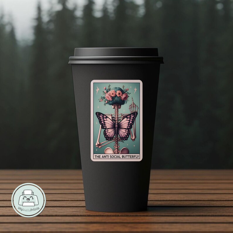 K&ouml;nnte beinhalten: Eine schwarze Kaffeetasse mit einem Aufkleber, der ein Skelett mit einem Schmetterling auf dem R&uuml;cken zeigt. Der Aufkleber tr&auml;gt den Text "The Anti Social Butterfly".