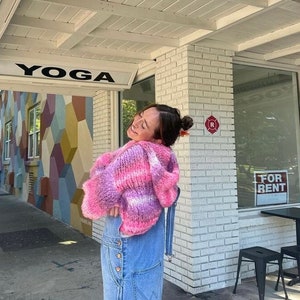 Peut inclure: Une personne portant un haut en crochet rayé rose et violet et une salopette en jean bleu se tient devant un bâtiment avec une pancarte indiquant "YOGA".