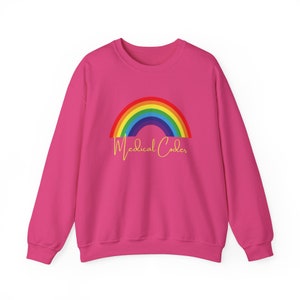 May include: A vibrant pink sweatshirt with a rainbow graphic in red, orange, yellow, green, blue, and purple. The words "Medical Coder" are written in a cursive font below the rainbow. The sweatshirt has a crew neck.
