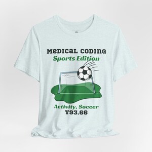 May include: A light blue t-shirt featuring the black text MEDICAL CODING, green text Sports Edition, a graphic of a football entering a goal net on a green patch, and the green text Activity, Soccer Y93.66 printed on the front centre.