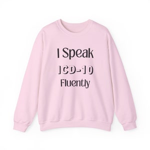 Puede incluir: Sudadera rosa claro con el texto negro "I Speak ICD-10 Fluently". La sudadera tiene mangas largas y cuello redondo. El texto está centrado en la parte delantera de la prenda.