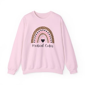 Peut inclure: Un sweat-shirt rose clair avec un motif arc-en-ciel. La couche supérieure de l'arc-en-ciel est imprimée léopard, avec des rayures roses et des cœurs noirs. Le texte "Medical Coder" est imprimé en dessous.