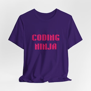 May include: A purple t-shirt with the words "CODING NINJA" in pink, pixelated font. The short-sleeved shirt is made of a soft material and is displayed on a white background. The text is centered on the front of the shirt.