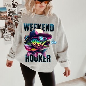 May include: A gray sweatshirt with the text "Weekend Hooker" and a colorful cartoon fish wearing sunglasses and a baseball cap.