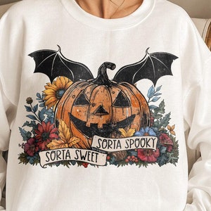 May include: White sweatshirt with a graphic of a jack-o'-lantern with bat wings and flowers. The text "Sorta Sweet" and "Sorta Spooky" is printed on a banner below the pumpkin.