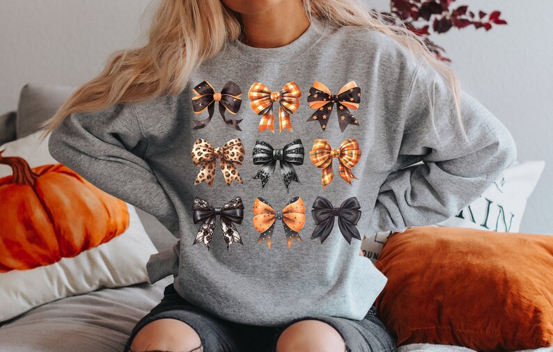 May include: A grey sweatshirt featuring a pattern of orange and black bows. The bows are in various styles, including polka dots, plaid, and leopard print.