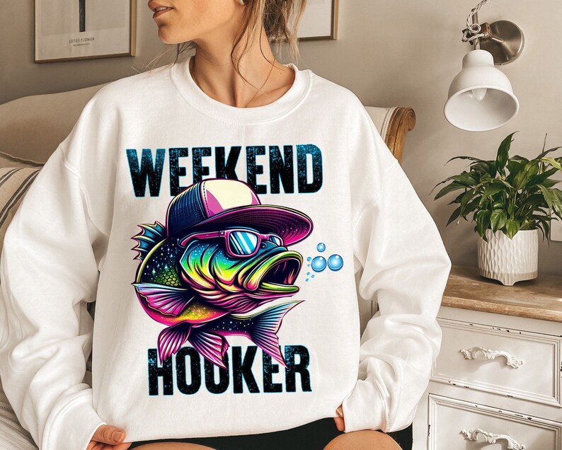 May include: White sweatshirt with a colorful graphic of a fish wearing sunglasses and a hat. The text "Weekend Hooker" is printed on the sweatshirt.