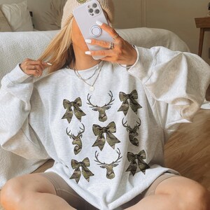 May include: A gray sweatshirt with a camouflage print of bows and deer heads.