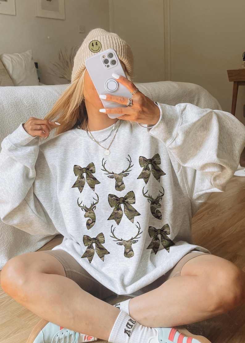 May include: A gray sweatshirt with a camouflage print of bows and deer heads.