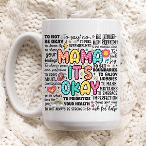May include: White ceramic mug with a colorful design that says "Mama it's okay" and includes a list of affirmations for self-care, such as "to not say no", "to enjoy the silence", "to set boundaries", "to prioritize your health", and "to ask for help".