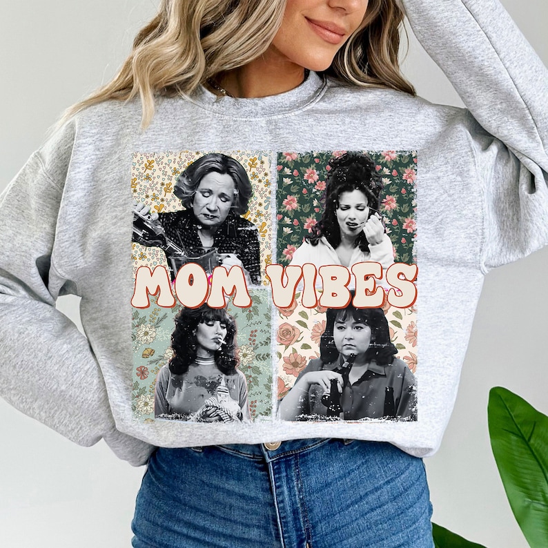 May include: Gray sweatshirt with a vintage-style graphic featuring four women's faces and the text "MOM VIBES" in colorful letters. The graphic is surrounded by floral patterns.