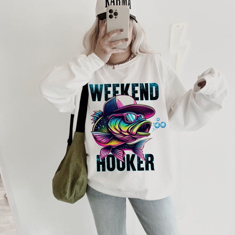 May include: White sweatshirt with a colorful graphic of a fish wearing sunglasses and a hat. The text "Weekend Hooker" is printed below the fish.