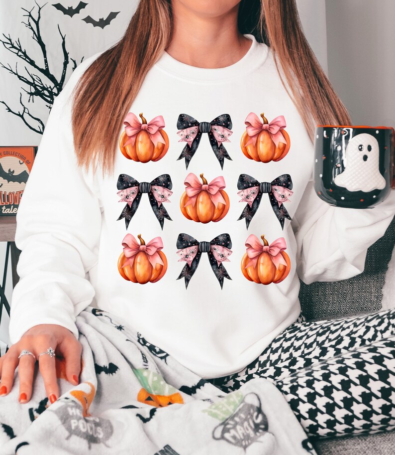 Puede incluir: Sudadera blanca con un patr&oacute;n de calabazas naranjas con lazos rosas y negros.