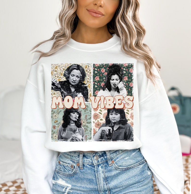 May include: White sweatshirt with a vintage-style graphic featuring four women and the text "MOM VIBES". The graphic is surrounded by floral patterns.
