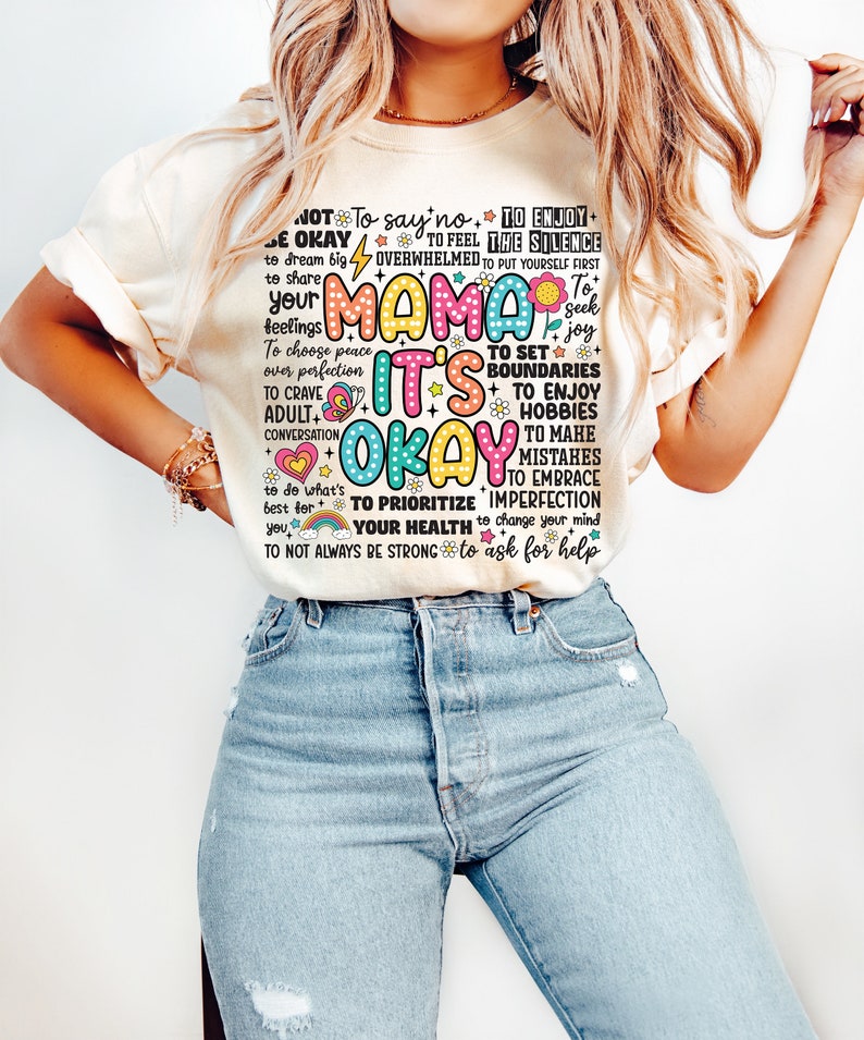 May include: A white t-shirt with a colorful graphic print that says "Mama It's Okay" and includes phrases like "To enjoy the silence", "To set boundaries", "To prioritize your health", and "To not always be strong".
