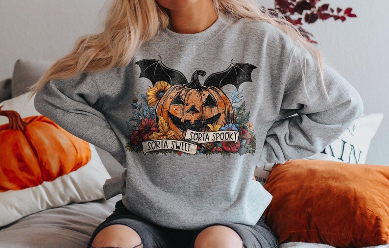 May include: Gray sweatshirt with a graphic of a pumpkin with bat wings and flowers. The text "Sorta Sweet" and "Sorta Spooky" is printed on the sweatshirt.