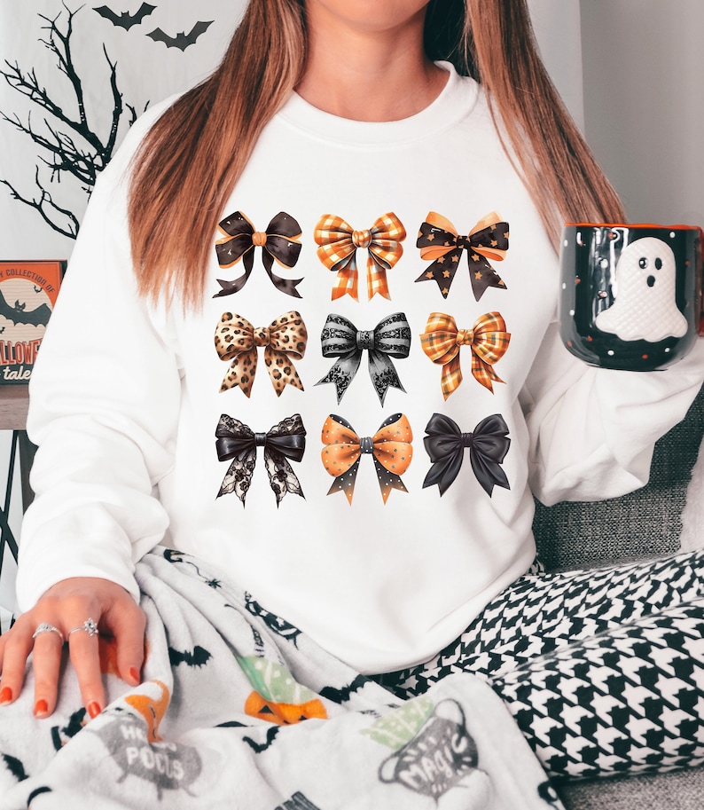 May include: A white sweatshirt featuring a design of nine black, orange and brown bows. The bows have various patterns, including polka dots, plaid and leopard print.