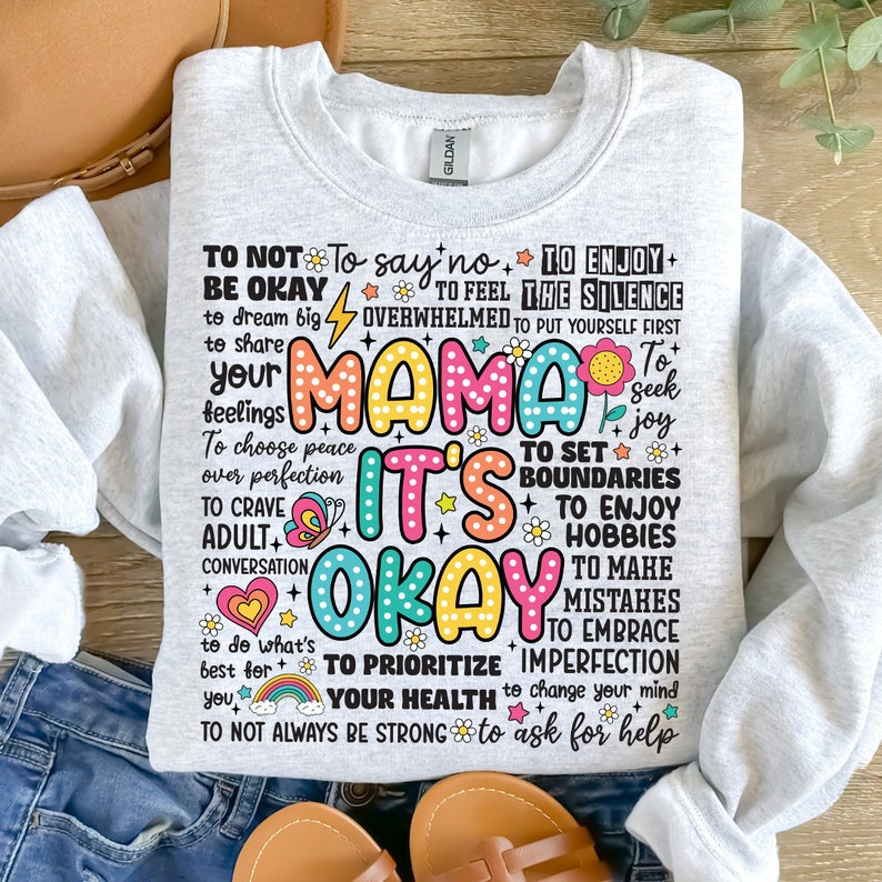 May include: A gray sweatshirt with a colorful graphic print that says "Mama It's Okay" and includes a list of affirmations for self-care and well-being.