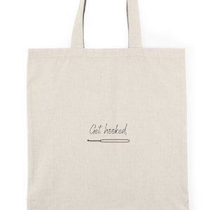 May include: A white canvas tote bag with black handles and the text "Get hooked" with a small drawing of a crochet hook.