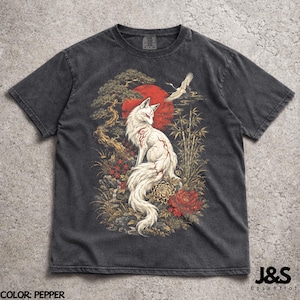 Puede incluir: Camiseta gris oscuro con un zorro blanco con marcas rojas, sobre un sol rojo y elementos de flora japonesa. El diseño incluye una grulla y bambú. El texto "J&S Essential" está en la esquina inferior derecha. El color de la camiseta es "Pepper".