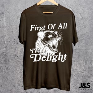 May include: A brown t-shirt with a white graphic of an animal with the text "First Of All I'm A Delight".