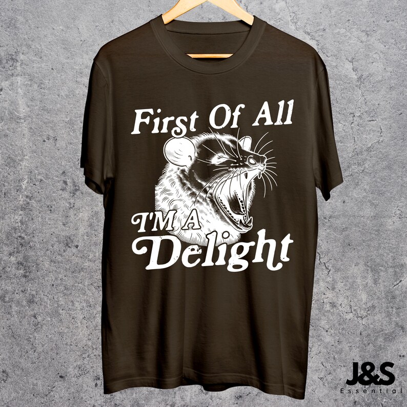 May include: A brown t-shirt with a white graphic of an animal with the text "First Of All I'm A Delight".