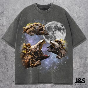 Pode incluir: Camiseta cinza escuro com um gráfico de três tartarugas mordedoras, uma lua cheia e um fundo estrelado. A camiseta tem gola redonda e mangas curtas. O texto "J&S Essential" está no canto inferior direito.