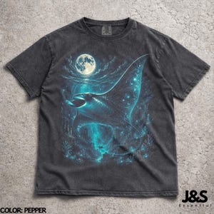 May include: Pepper-colored t-shirt featuring a detailed illustration of a manta ray swimming in a moonlit ocean. The design includes a full moon, coral, and other aquatic elements, with the text "J&S Essential" at the bottom.