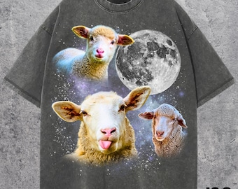 Puede incluir: Camiseta gris oscuro con un diseño caprichoso de tres ovejas, una luna llena y un fondo estrellado. Las ovejas tienen caras expresivas, una de ellas sacando la lengua. El texto "J&S Essential" está en la parte inferior.