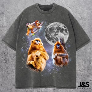 May include: Dark gray t-shirt featuring a graphic of three golden snub-nosed monkeys with a full moon in the background. The monkeys are in a starry space scene. The shirt has a relaxed fit.
