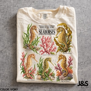 以下が含まれることがあります： FIELD GUIDE TO SEAHORSESというタイトルのグラフィックプリントが施されたアイボリーのTシャツ。Lined、Bargibant's Pygmy、Big-belly、Thorny、Long-snouted、Tiger-tailの6種類のタツノオトシゴが、色鮮やかなサンゴや海藻と共に描かれています。