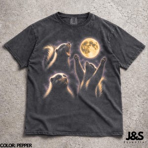 Puede incluir: Camiseta color pimienta con un gráfico de tres zorrillos mirando una luna llena. Los zorrillos están en varias poses, uno aullando y otro con las patas levantadas. La camiseta tiene un aspecto vintage y desgastado.