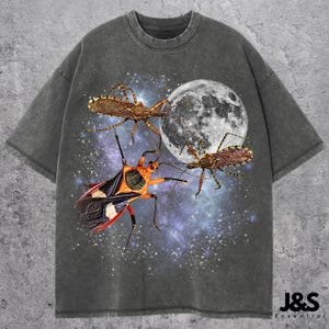 May include: Dark grey t-shirt with a graphic of three insects set against a full moon and a starry sky. The insects are brown, orange, black, and white. The shirt has the text "J&S Essential" at the bottom.