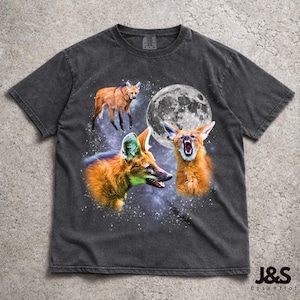 Pode incluir: T-shirt cinzenta escura com um design gráfico de três lobos-guará, uma lua cheia e um fundo estrelado. Os lobos-guará são retratados em tons de castanho e laranja. O texto "J&S Essential" está no canto inferior direito.