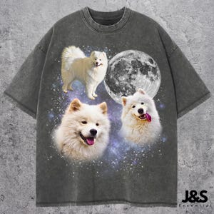 May include: Dark gray t-shirt featuring a graphic design of three fluffy white Samoyed dogs and a full moon against a starry background. The shirt has a vintage, washed-out look. The text "J&S Essential" is printed at the bottom right.