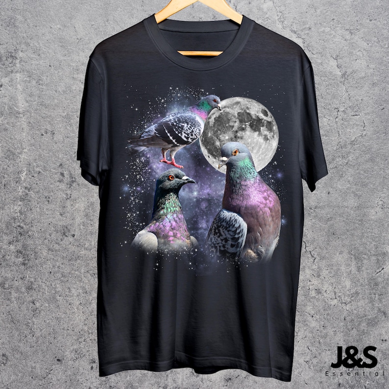 Puede incluir: Camiseta negra con un gr&aacute;fico de tres palomas con plumas iridiscentes sobre un cielo estrellado y una luna llena. La camiseta tiene el texto "J&S Essential" en la parte inferior.