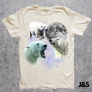 May include: Cream-colored t-shirt featuring a design of polar bears and a full moon. The graphic includes three polar bear illustrations and a detailed depiction of the moon. The shirt has a crew neck and short sleeves. The brand name "J&S Essential" is printed at the bottom right.