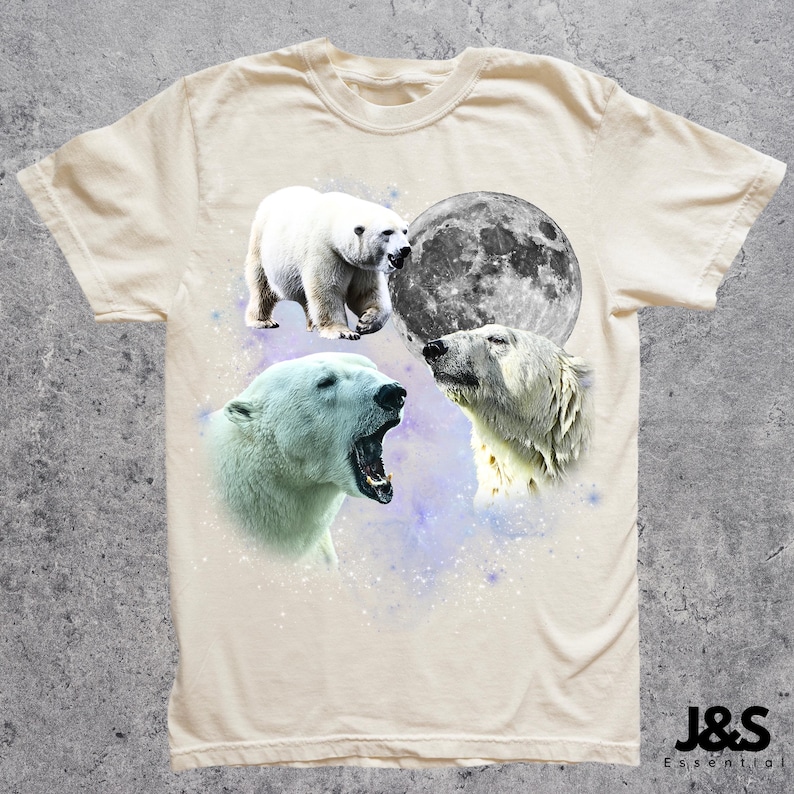 May include: Cream-colored t-shirt featuring a design of polar bears and a full moon. The graphic includes three polar bear illustrations and a detailed depiction of the moon. The shirt has a crew neck and short sleeves. The brand name "J&S Essential" is printed at the bottom right.