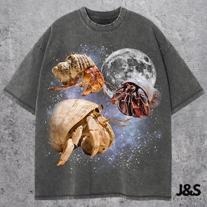 May include: Dark gray t-shirt featuring a graphic of three hermit crabs with a full moon and starry background. The crabs are in shades of orange, brown, and beige. The text "J&S Essential" is at the bottom right.