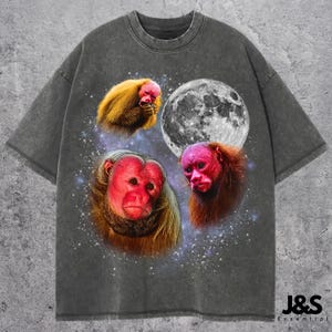 May include: Dark gray t-shirt featuring a graphic design of three monkeys with red faces and yellow fur, a full moon, and a starry background. The shirt has a crew neck and short sleeves. The brand name "J&S Essential" is printed on the bottom right.