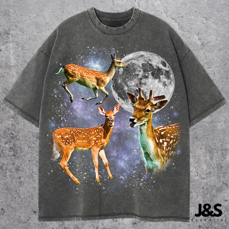 May include: Dark gray t-shirt featuring a graphic of three deer with a full moon and a starry background. The deer are brown with white spots. The text "J&S Essential" is at the bottom right.
