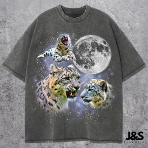 Può includere: T-shirt grigio scuro con una grafica di tre leopardi delle nevi, una luna piena e uno sfondo stellato. Un leopardo delle nevi ruggisce. Il testo "J&S Essential" è in basso a destra.
