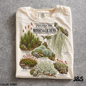 May include: An ivory t-shirt featuring a graphic titled Field Guide to Mosses & Lichens. The print displays detailed illustrations of Common Haircap Moss, Old Man's Beard Lichen, Pincushion Moss, Fire Moss, Reindeer Lichen, and British Soldiers Lichen.