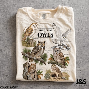 Può includere: Una t-shirt color avorio con una stampa grafica intitolata Field Guide to Owls. Il design mostra illustrazioni di un barbagianni, un gufo delle nevi, un gufo della Virginia, un allocco, un assiolo e una civetta con i nomi in nero.
