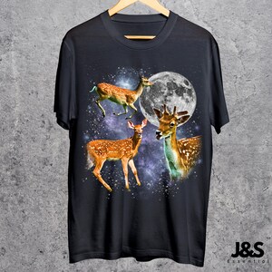 May include: Dark navy blue t-shirt featuring a graphic of three deer with a full moon and a starry background. The deer are brown with white spots. The text "J&S Essential" is at the bottom right.