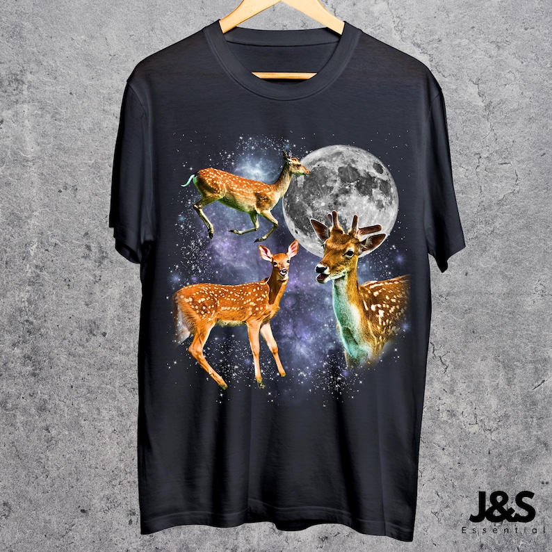 May include: Dark navy blue t-shirt featuring a graphic of three deer with a full moon and a starry background. The deer are brown with white spots. The text "J&S Essential" is at the bottom right.
