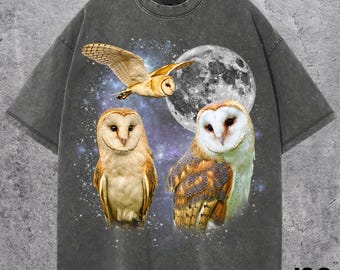 May include: Dark gray t-shirt featuring a graphic of three owls, a full moon, and a starry night sky. The owls are depicted in shades of brown, white, and gold. The shirt has a vintage, distressed look.