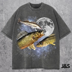 Könnte beinhalten: Ein anthrazitfarbenes Kurzarm-T-Shirt mit einem Grafikdruck von drei Fischen, die vor einem großen weißen Mond und einer sternenklaren Galaxie schwimmen. In der unteren rechten Ecke steht der Text J&S Essential in schwarzer Schrift.