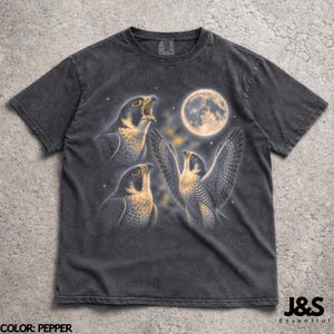 Könnte beinhalten: Dunkelgraues T-Shirt mit einer detaillierten Illustration von drei Falken unter einem Vollmond. Die Falken sind mit offenen Flügeln und Schnäbeln dargestellt, vor einem sternenklaren Nachthimmel. Das T-Shirt hat einen Vintage-Look.