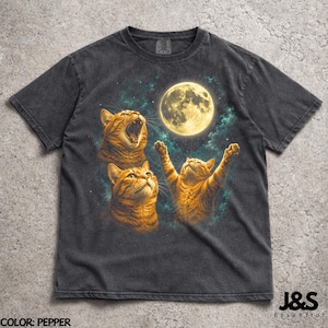 Op de afbeelding: Donkergrijze t-shirt met een print van drie oranje katten die naar een volle maan in een sterrenhemel kijken. Eén kat gaapt, een andere kijkt omhoog en de derde heeft zijn poten omhoog. De tekst "J&S Essential" staat onderaan.